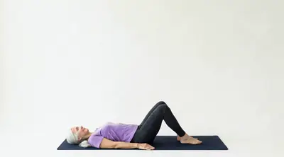 Looping video demonstration of the Knee To Chest Stretch exercise — a physician-designed movement performed on a mat in a bright studio.
