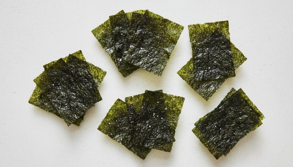 Flat-lay photo of roasted seaweed snack sheets with a dry, crisp texture on a light background.