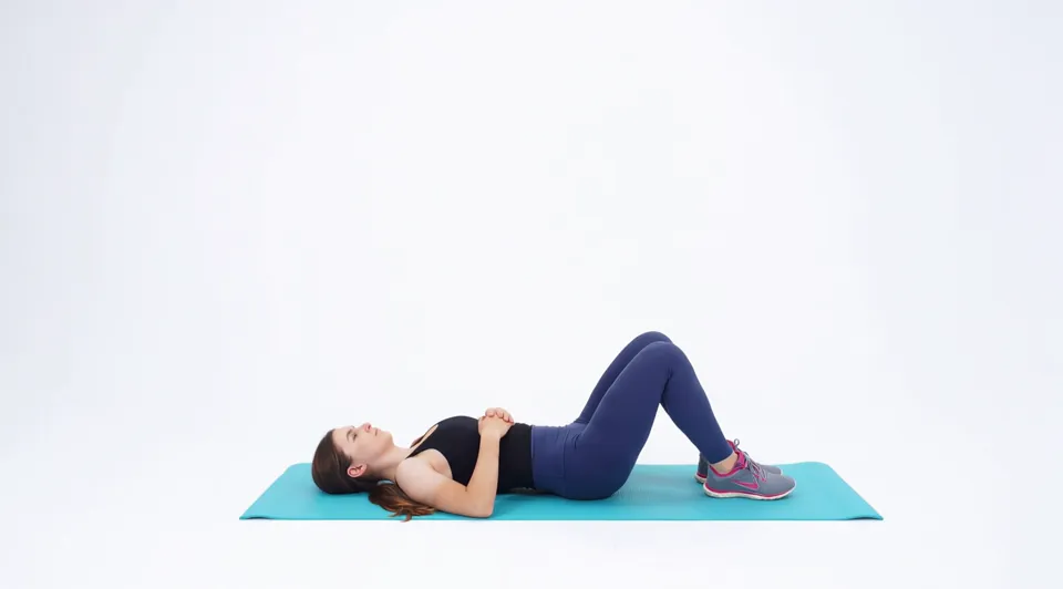 Looping video demonstration of the Supine Knee Side-to-Side exercise — a physician-designed movement performed on a mat in a bright studio.