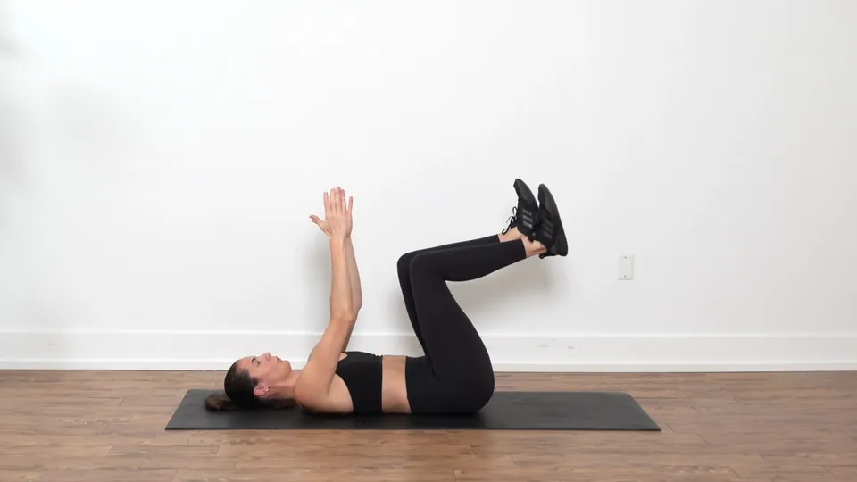 Woman lying on her back performing the Dead Bug exercise, extending one arm overhead and the opposite leg long
